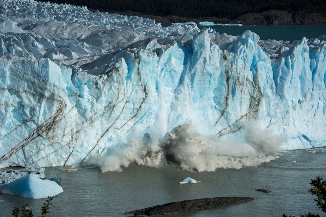 Kusy ledu se odtrhují z čela ledovce a padají do zpěněné vody.